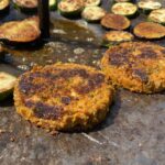 Fehérbabos hamburger pogácsa átfordítás után sütés közben cukkinival és padlizsánnal szabadtéren parázs felett tárcsalapon sütve
